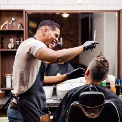 Rear view shot of man client visiting haidresser and hairstylist in barber shop.